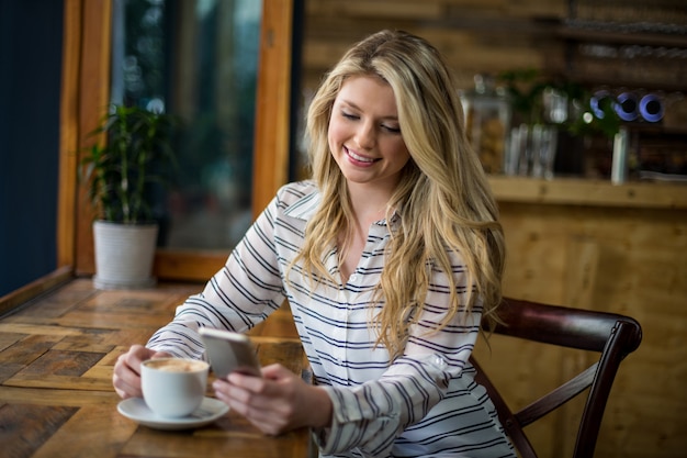 Smiling woman using mobile phone while having coffee