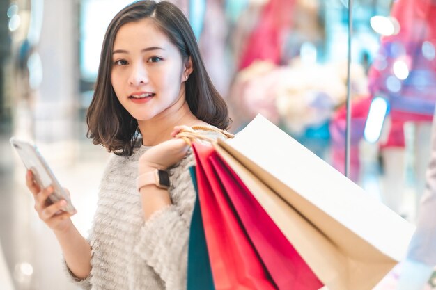 Photo smiling woman using mobile phone while holding shopping bags in store