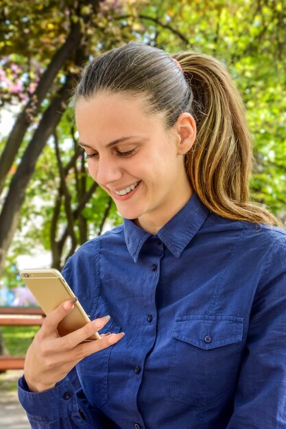 Foto donna sorridente che usa il telefono contro un albero