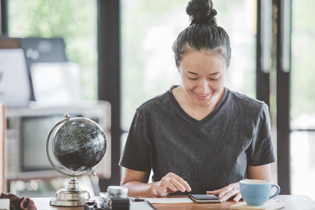 写真 オフィスに座っている間スマートフォンを使っている笑顔の女性