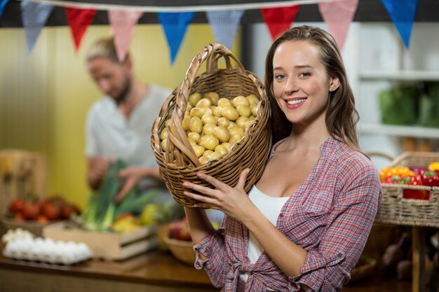 Smiling woman vendor holding a basket if potatoes in grocery store