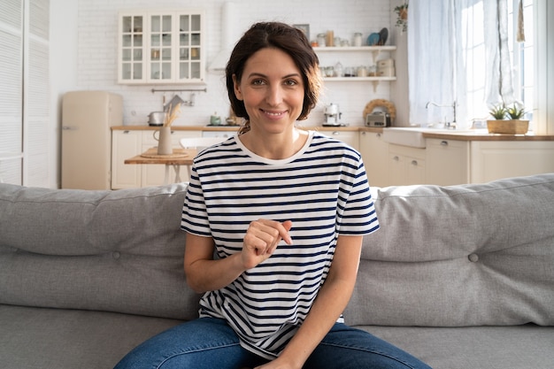 Smiling woman vlogger influencer recording new content to vlog, looking at webcam, sitting on couch.