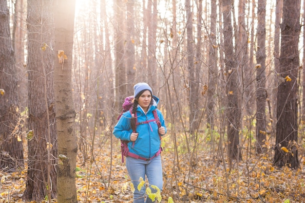 秋の自然な背景の上にバックパックで歩く笑顔の女性。