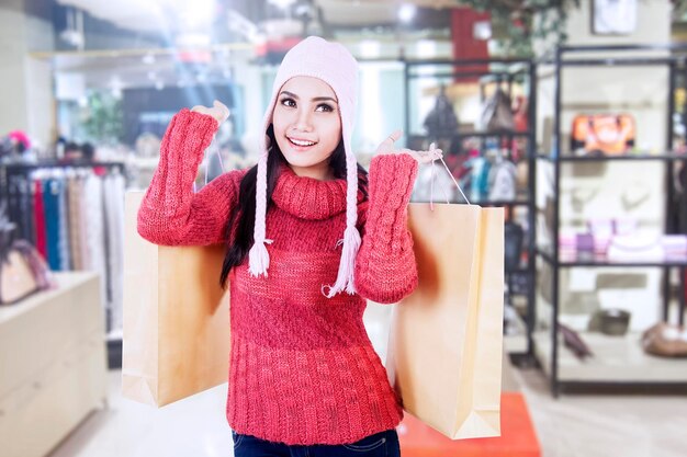 Photo smiling woman in warm clothes holding shopping bags while standing in store