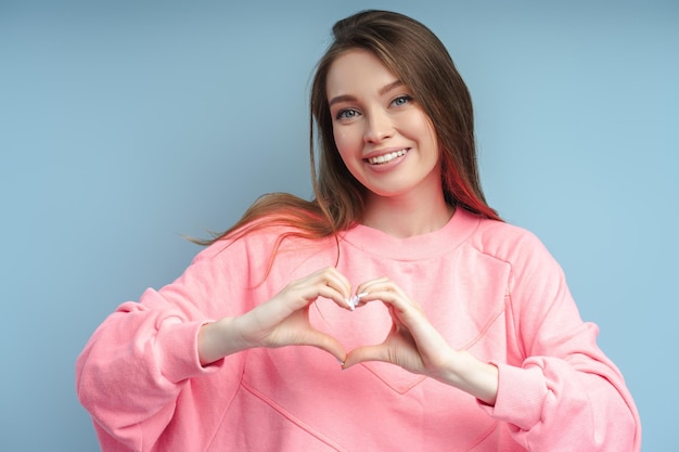 Photo smiling woman wearing pink sweatshirt with toothy smile gesturing heart with fingers