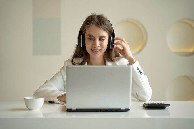 ワイヤレスヘッドフォンをかぶった笑顔の女性がオフィスのラップトップコンピュータでビデオコールをします