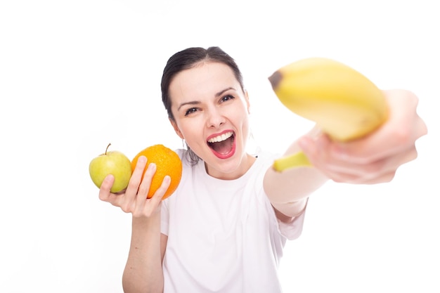 smiling woman in white tshirt holding apple orange and banana in her hands white background