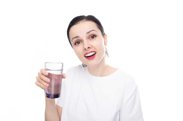 smiling woman in a white tshirt holds a glass of water in her hand white studio background