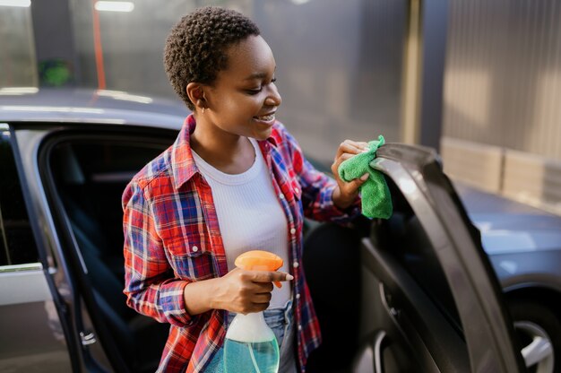 Smiling woman wipes a car with a rag, hand auto wash station. Car-wash industry or business. Female person cleans her vehicle from dirt outdoors