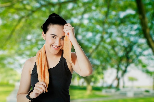 Photo smiling woman wiping sweat after workout at park