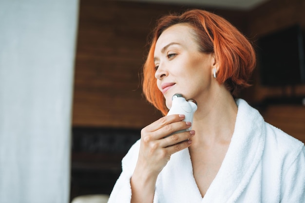 Smiling woman with clean fresh face and hands doing fasial massage with microcurrent facial massager