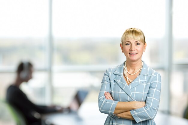 Smiling woman with crossed arms. Mature woman with crossed arms standing on office window.