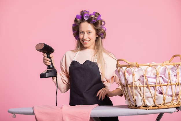 A smiling woman with curled rollers in her hair holds a steamer to iron shirts portrait of a beautif