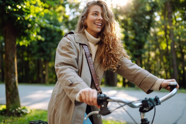 Foto donna sorridente con capelli ricci in cappotto va in bicicletta nel parco soleggiato stile di vita rilassati il concetto di natura