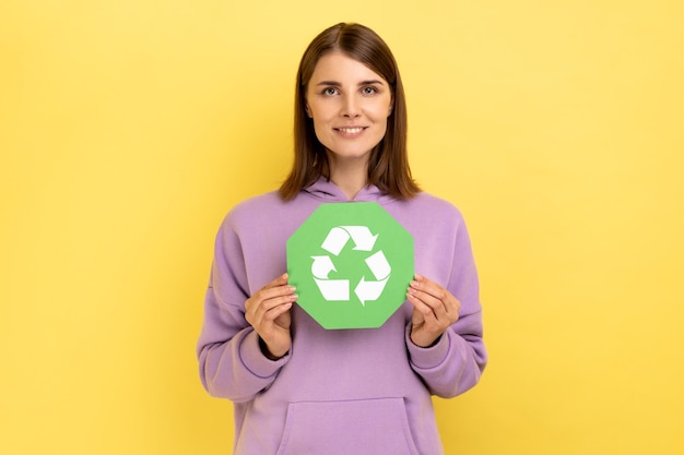 Smiling woman with dark hair holding in hands green recycling sing ecology concept looks at camera
