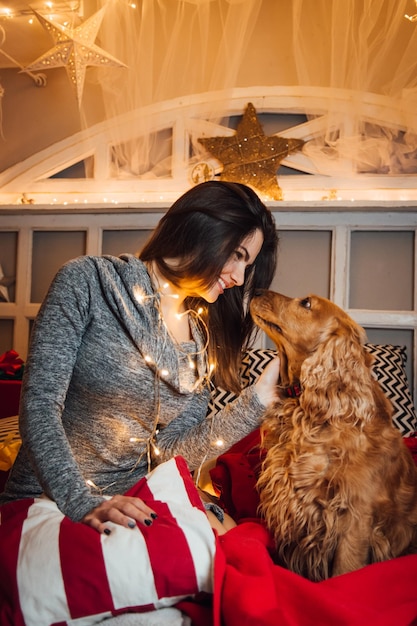 クリスマスの間に家でベッドに座っている犬と笑顔の女性