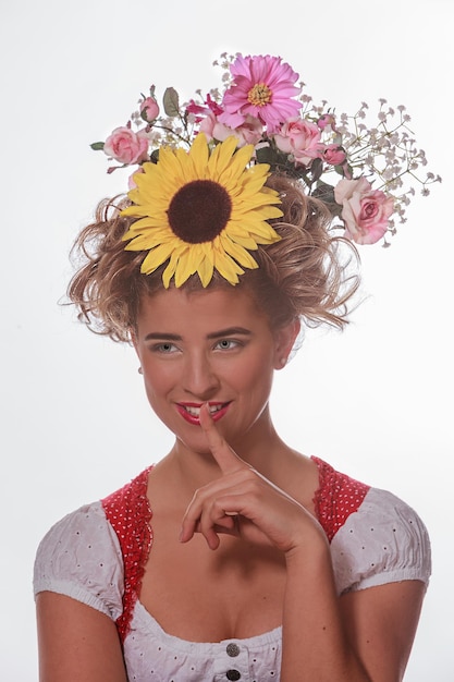 Smiling woman with finger on lips wearing flowers on hair against white background