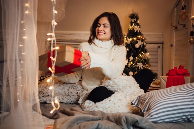Smiling woman with gift box sitting at home during christmas
