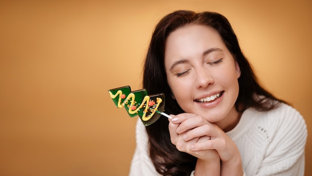 黄色の背景の上の緑のロリポップと笑顔の女性クリスマスのお菓子のコンセプト