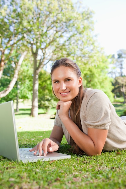 Smiling woman with her laptop while lying on the lawn