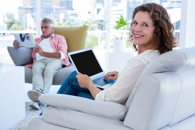 Smiling woman with laptop while mature man reading newspaper