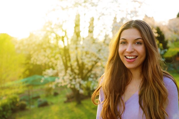 Smiling woman with long hair posing near blooming tree