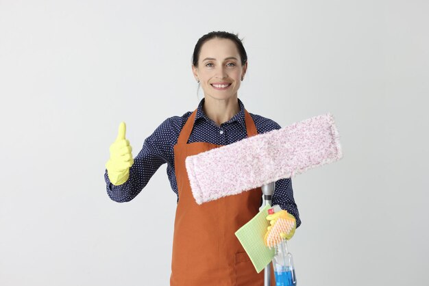 Улыбающаяся женщина со шваброй, держащая большой палец вверх, дает рекомендации по уборке концепции клининговых компаний