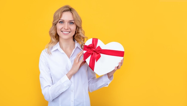 Smiling woman with present heart box on yellow background