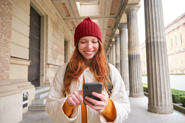 마을 searchi 주위를 산책하는 동안 휴대 전화 응용 프로그램을 사용하여 빨간 머리 관광객과 웃는 여자