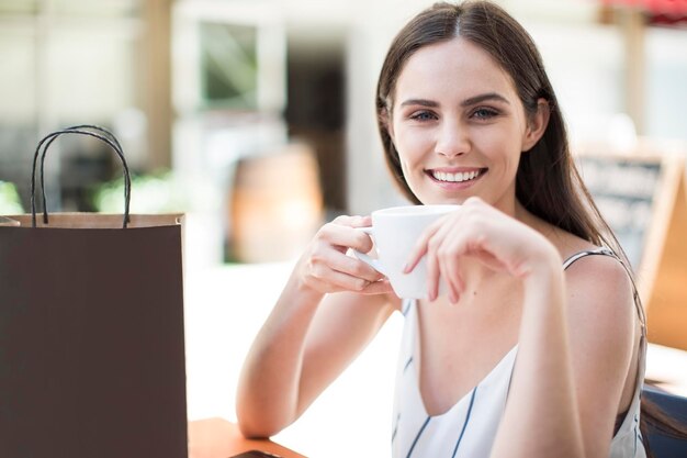 Smiling woman with shopping bag enjoying coffee at cafe