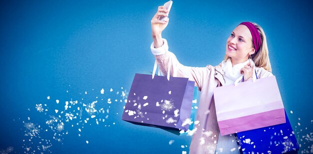 Photo smiling woman with shopping bags taking selfies against blue background