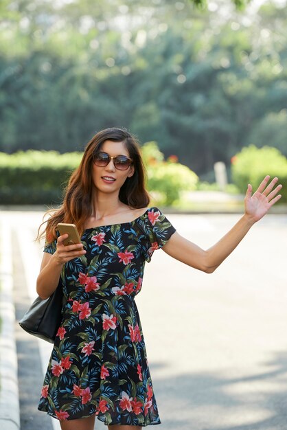 Smiling woman with smartphone hailing taxi