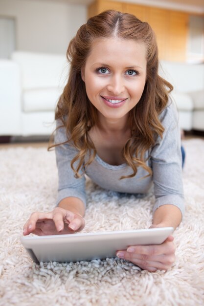 Smiling woman with tablet laying on the carpet