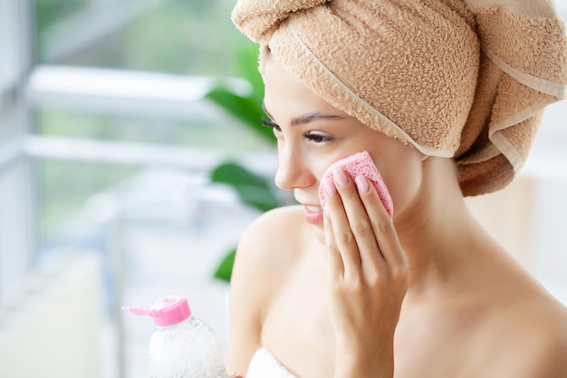 Smiling woman with wrapped in towel head using face sponge