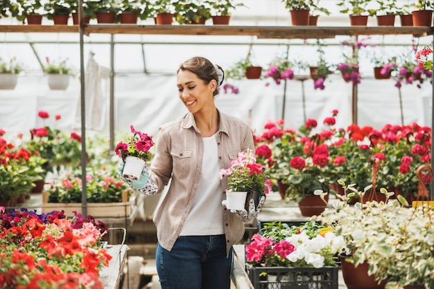 Smiling woman working in a garden center and taking care of potted plants and flowers.