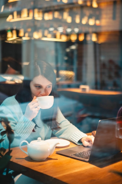 ハンバーガーを食べるお茶を飲むレストランでラップトップに取り組んでいる笑顔の女性