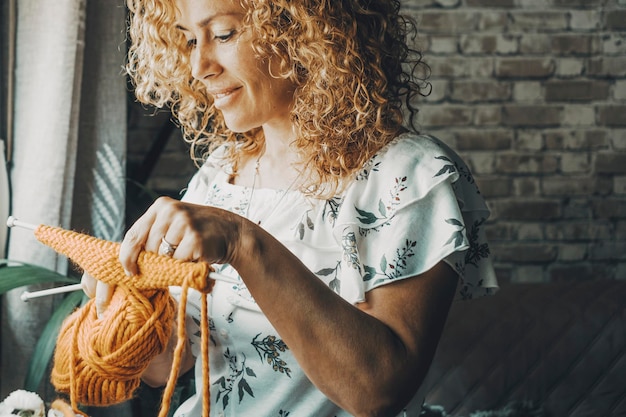 Smiling woman working with knitting rok hobby at home Indoor leisure activity time Adult female smile Curly hair Young mature lady people doink knit activity and enjoying time alone Window light