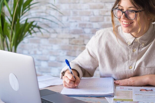 Smiling woman write notes watch webinar study work on laptop young student learning computer course listening lecture training interpreter online teacher translating classxA