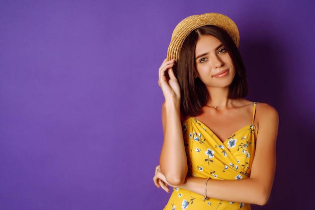 Smiling woman in yellow dress and hat posing purple background fashion style