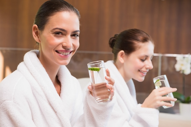 Smiling women in bathrobes drinking water