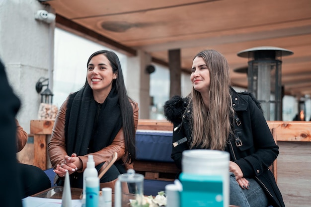 Smiling women sitting outdoors with beauty products on table and chatting