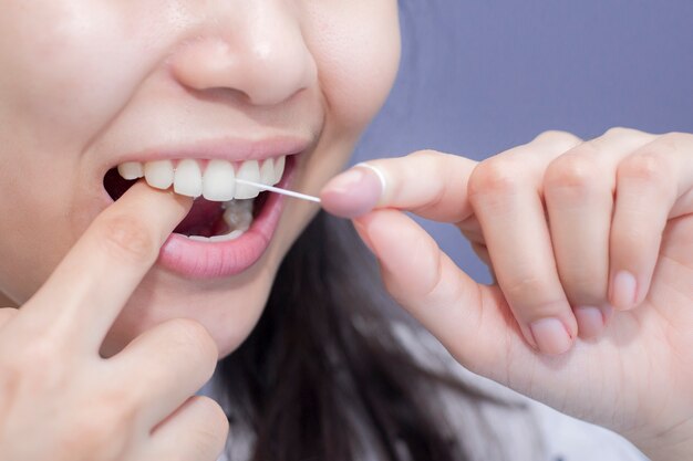 Le donne sorridenti usano i denti sani bianchi del filo interdentale