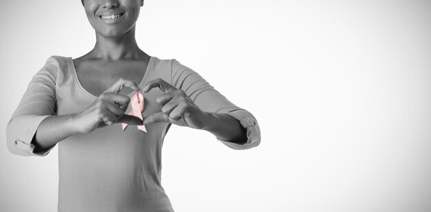 Улыбающиеся женщины в розовой рубашке делают сердце пальцами вокруг розовой ленты
