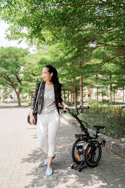 La donna lavoratrice sorridente cammina sulla sua bici pieghevole attraverso il parco