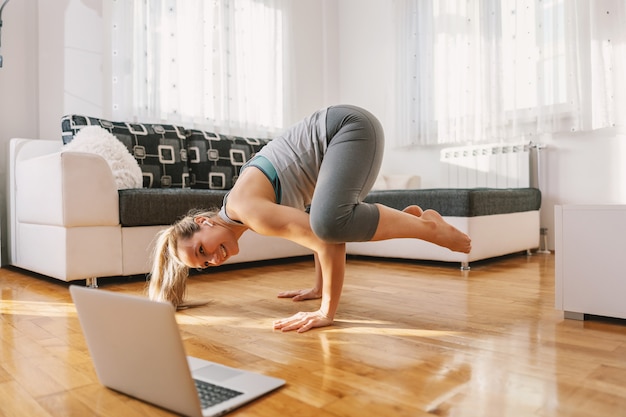 Smiling yoga instructor in crow yoga pose having online class over laptop