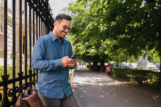 Smiling young adult business man getting a notification on phone resting outside