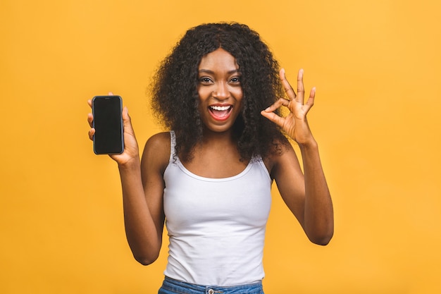 Smiling young African American black woman holding blank screen mobile phone and showing ok sign