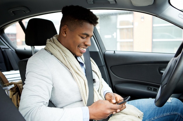 車を運転している間携帯電話を見ている笑顔の若いアフリカ系アメリカ人ビジネスマン