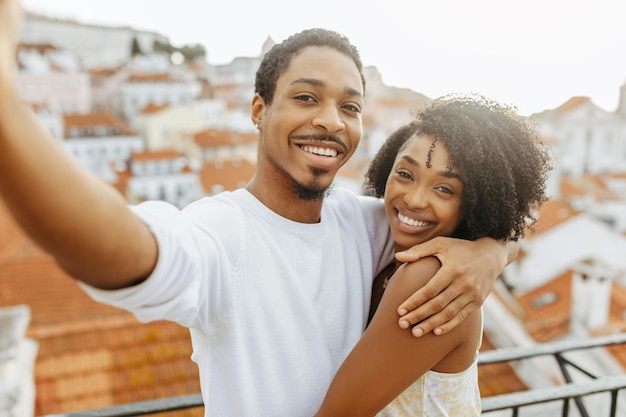 Smiling young african american guy hug lady in dress taking selfie in city enjoy date and travel