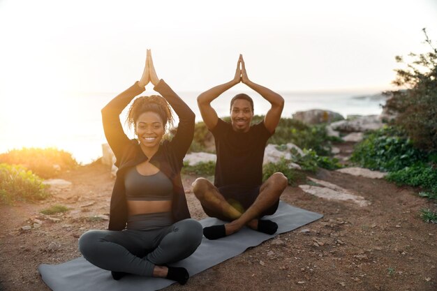 Smiling young african american lady and man in sportswear sit enjoy workout practice yoga in morning